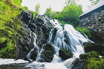 A beautiful waterfall cascades over mossy rocks in a serene green forest with clear blue skies above. HD wallpaper