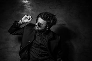 Black and white portrait of a fashionable man in sunglasses and suit posing confidently indoors. HD wallpaper