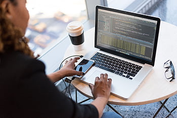Black woman programming on a laptop with coffee, smart, and glasses on a desk in an office. HD wallpaper