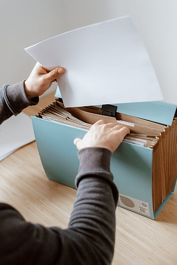Hands organizing documents in a blue office file organizer on a wooden table indoors. HD phone wallpaper