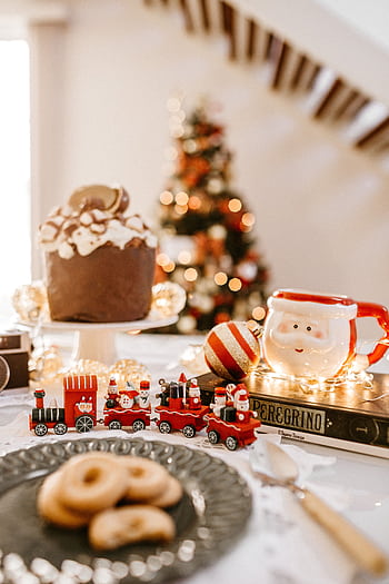 Cozy indoor Christmas scene with Santa mug, treats, and decorations. HD phone wallpaper