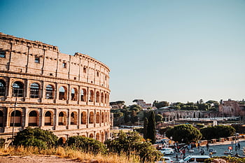 The iconic Colosseum in Rome, a historic amphitheater surrounded by urban scenery on a bright day. HD wallpaper