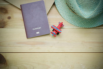 Flat lay of a passport, straw hat, and toy airplane on a wooden surface. HD wallpaper