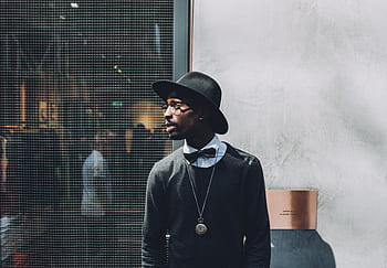 Chic portrait of a fashionable man wearing a hat and bow tie against a textured wall. HD wallpaper