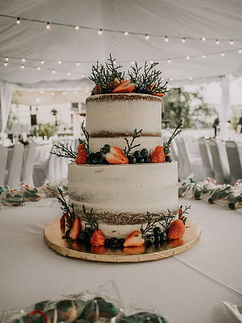 A two-tier naked wedding cake adorned with fresh strawberries and blueberries in a decorated reception tent. HD phone wallpaper