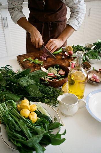 Adult preparing salad with fresh vegetables, knife, and olive oil in kitchen setting. HD phone wallpaper