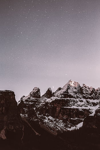 Majestic snow-covered mountain peaks illuminated under a starry night sky, creating a serene and breathtaking landscape. HD phone wallpaper