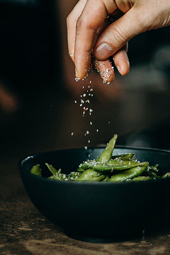A hand sprinkles salt on fresh edamame, showcasing a delicious and healthy cooking moment. HD phone wallpaper