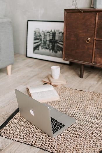A serene workspace with a laptop, open book, and coffee cup on a textured rug, ideal for remote work. HD phone wallpaper