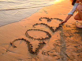A woman draws '2023' in the sand during a beautiful beach sunset, symbolizing new beginnings. HD wallpaper