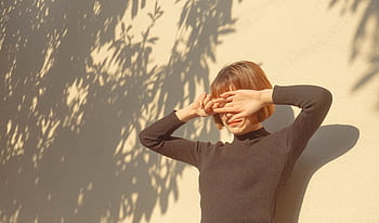 A stylish woman covers her eyes from the sun, enjoying a bright outdoor day. HD wallpaper