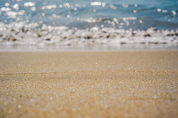 Close-up of sandy beach with ocean waves and sparkling water in the background. HD wallpaper