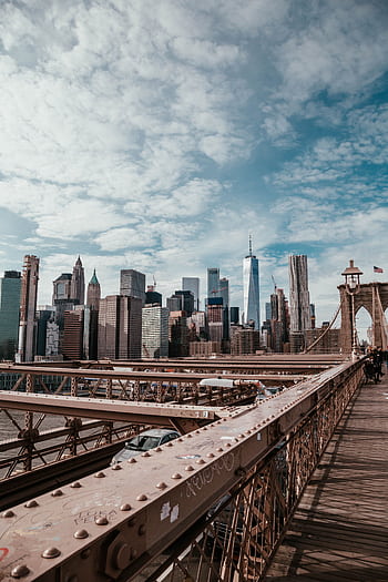A breathtaking view of the New York City skyline from the Brooklyn Bridge, featuring iconic skyscrapers under a cloudy sky. HD phone wallpaper