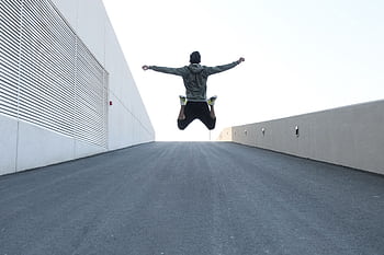 Man jumping on urban road with arms spread wide in Dubai, showcasing dom and energy. HD wallpaper