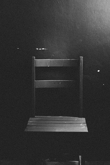 Black and white of an empty wooden chair with a dark background, showcasing minimalism. HD phone wallpaper