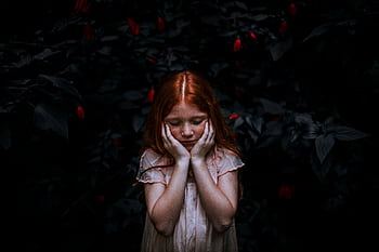 A young redhead girl in a thoughtful pose surrounded by dark foliage. HD wallpaper