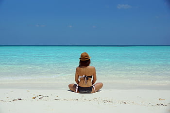 Rear view of a woman in a bikini and hat relaxing on a pristine beach in Maldives. HD wallpaper