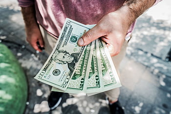 A person holding several twenty-dollar bills outdoors, depicting payment or financial transaction. HD wallpaper