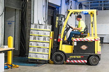A worker drives a Hyster forklift moving Joe IPA boxes in a warehouse. HD wallpaper