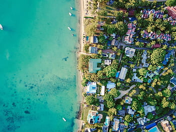 A stunning aerial view of a vibrant tropical coastal village with turquoise waters and lush greenery. HD wallpaper