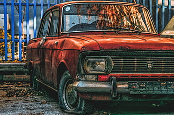 An atmospheric of a rust-covered vintage car parked in an urban outdoor space. HD wallpaper