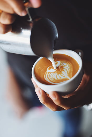 Close-up of barista pouring milk to create stunning latte art in a coffee shop setting. HD phone wallpaper