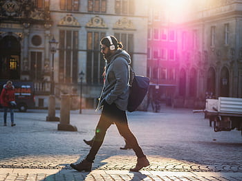 Man with heads walks down a sunlit urban street, casting a shadow on the cobblestones. HD wallpaper