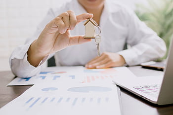 Real estate professional presenting a house model with keys, symbolizing property investment and ownership. HD wallpaper