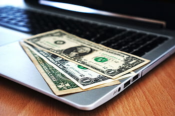 Close-up of US dollar bills placed on a laptop symbolizing digital finance and economy. HD wallpaper