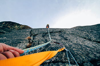 Capture the thrill of rock climbing with this dynamic low-angle shot showcasing determination and teamwork. HD wallpaper