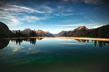 Serene dawn view of a mountain lake with clear reflections under a vibrant sky. HD wallpaper