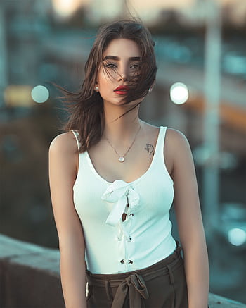 Stylish woman in white top posing outdoors with urban backdrop. HD phone wallpaper