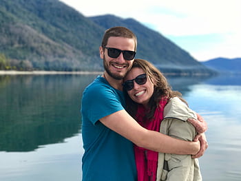 A joyful couple shares a warm embrace by a serene mountain lake, symbolizing love and togetherness. HD wallpaper