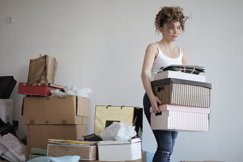 A young woman carrying boxes during a move into a new apartment, surrounded by packed belongings. HD wallpaper