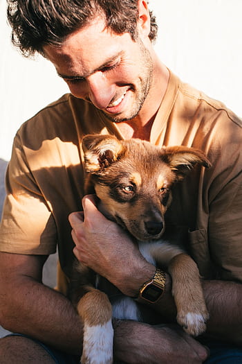 Smiling man embraces a cute puppy outside on a sunny day, expressing joy and companionship. HD phone wallpaper