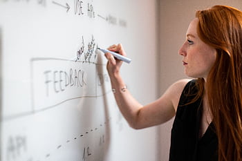 Focused woman writing on a whiteboard during a business planning session. HD wallpaper