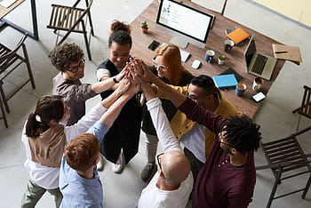 A diverse group of colleagues giving a high five during a corporate meeting indoors. HD wallpaper