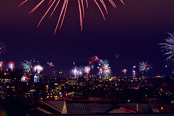 Vibrant fireworks light up the night sky over a city. Perfect for celebrations or festive events. HD wallpaper