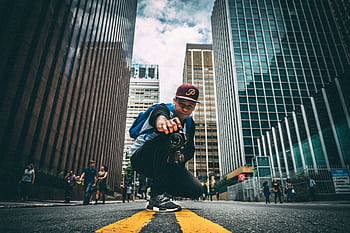 A young man with a camera kneels on a bustling city street, surrounded by skyscrapers. HD wallpaper