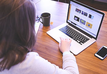 Person browsing the web on a MacBook at a wooden desk with a smart. HD wallpaper