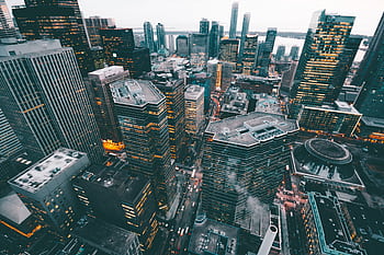 High-angle view of a bustling cityscape with skyscrapers and urban lights at dusk. HD wallpaper
