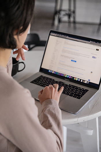 A professional woman uses a laptop while working remotely from home, focusing on online tasks. HD phone wallpaper
