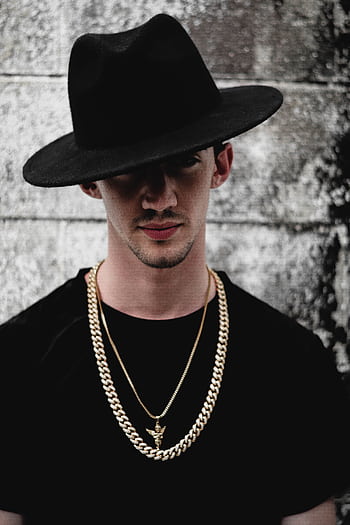 Portrait of a fashionable man wearing a black hat and gold chains against a textured background. HD phone wallpaper