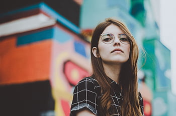 Portrait of a fashionable woman with glasses posing confidently outdoors in front of a vibrant mural. HD wallpaper