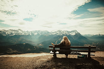Woman enjoys a peaceful view of snow-capped mountains from a bench, capturing the essence of nature's serenity. HD wallpaper