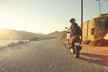 Woman riding scooter on scenic Greek road at sunrise, capturing adventure and travel vibes. HD wallpaper