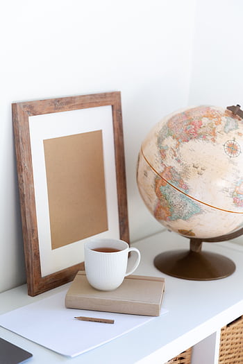 A serene home office setup featuring a globe, frame, and mug on a white desk, perfect for inspiration. HD phone wallpaper