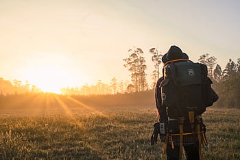A lone backpacker gazes at a sunrise over a foggy field, embracing adventure. HD wallpaper