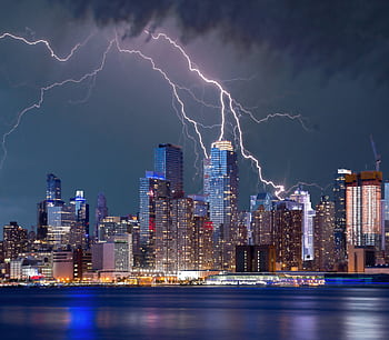 Thrilling lightning storm over a bustling urban skyline at night with stunning reflections on the waterfront. HD wallpaper