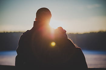 A romantic couple embraces with a beautiful lens flare at sunrise, creating a warm and intimate silhouette. HD wallpaper